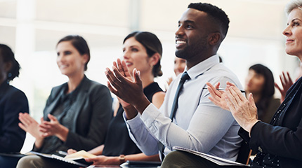 A group of people are seated in a classroom and are clapping while facing the front of the room.