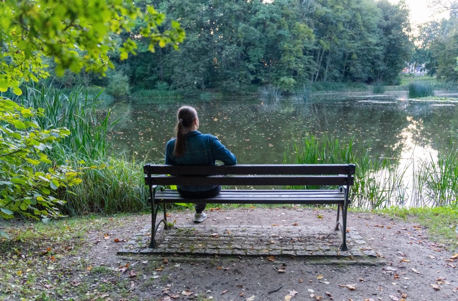 woman sitting on bench looking at trees and pond practicing mindfulness in nature