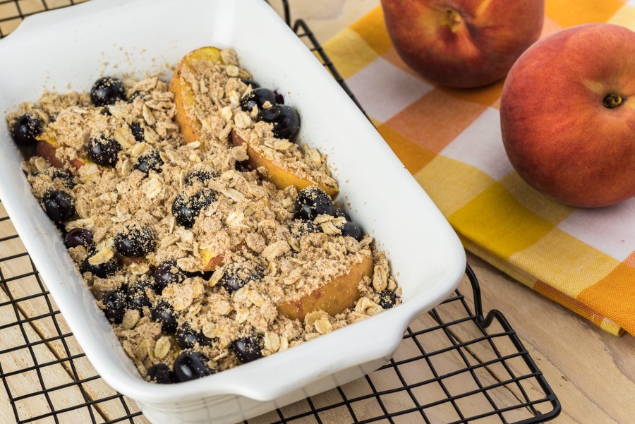 peach berry crisp cooling in a baking dish near fresh peaches