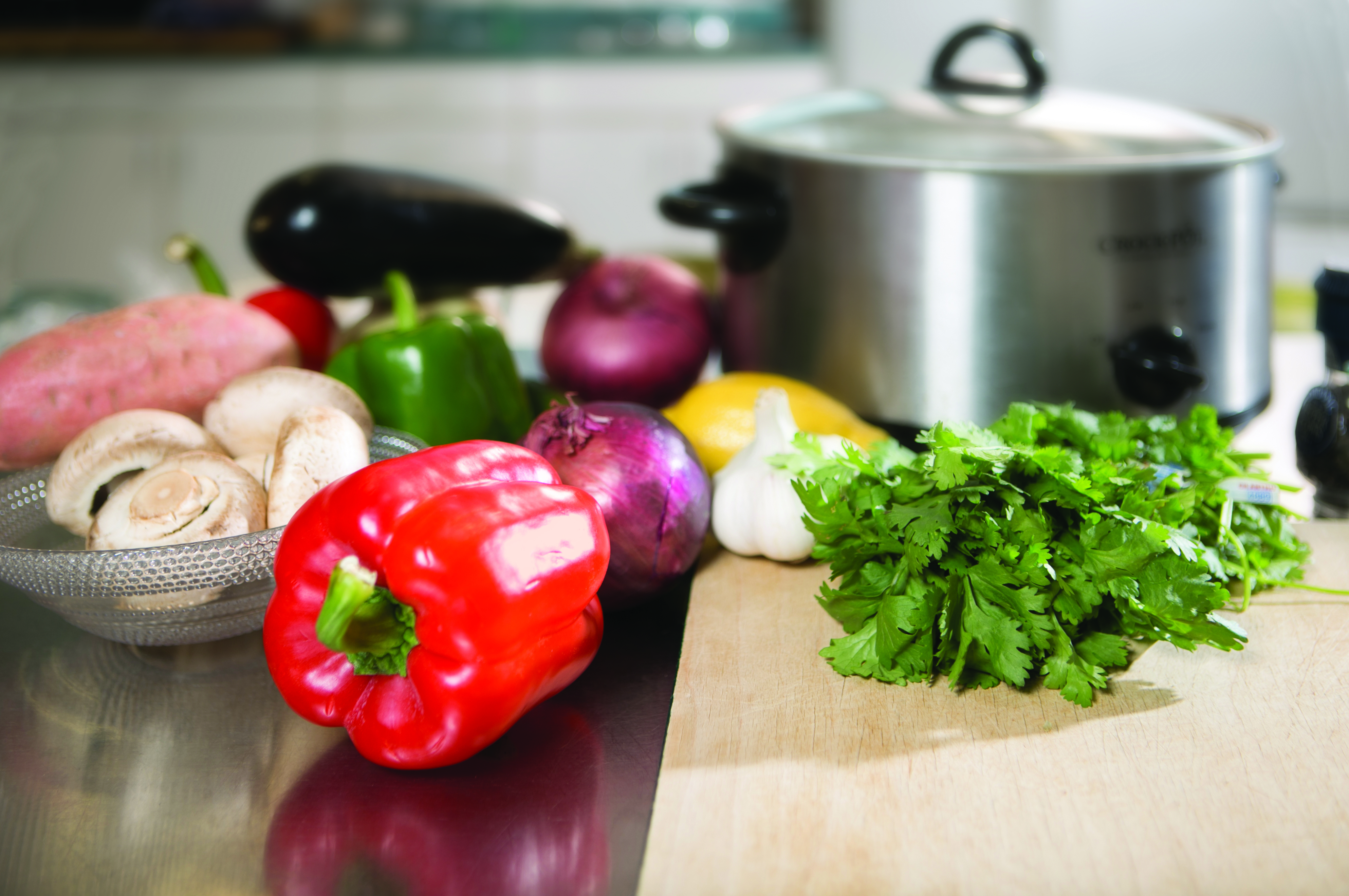 Various vegetables are shown on a cutting board in front of a crock-pot.