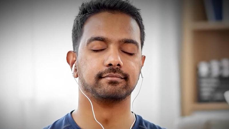 Close-up of a man with eyes closed and earbuds on.