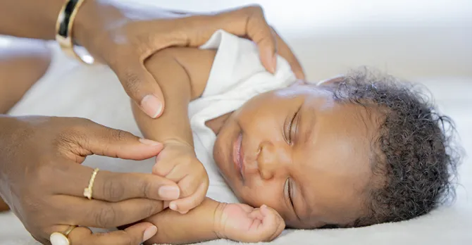 A baby peacefully sleeping on a soft surface, is being gently cared for by adult hands.