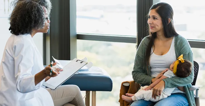 A new mom and her baby speak to a doctor in an exam room.