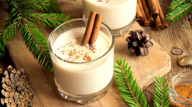 cup of eggnog on a wooden cutting board with pinecones and greenery