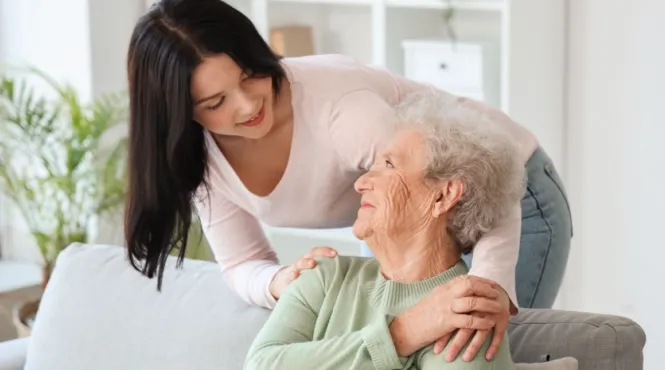 daughter standing behind a couch hugging grandmother while ensuring she is in a safe home