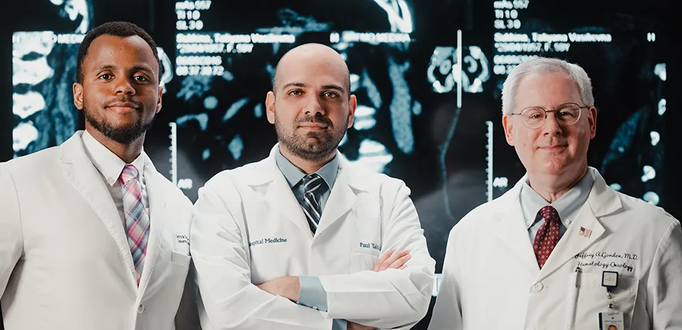 3 doctors are facing the camera in front of body scan films.