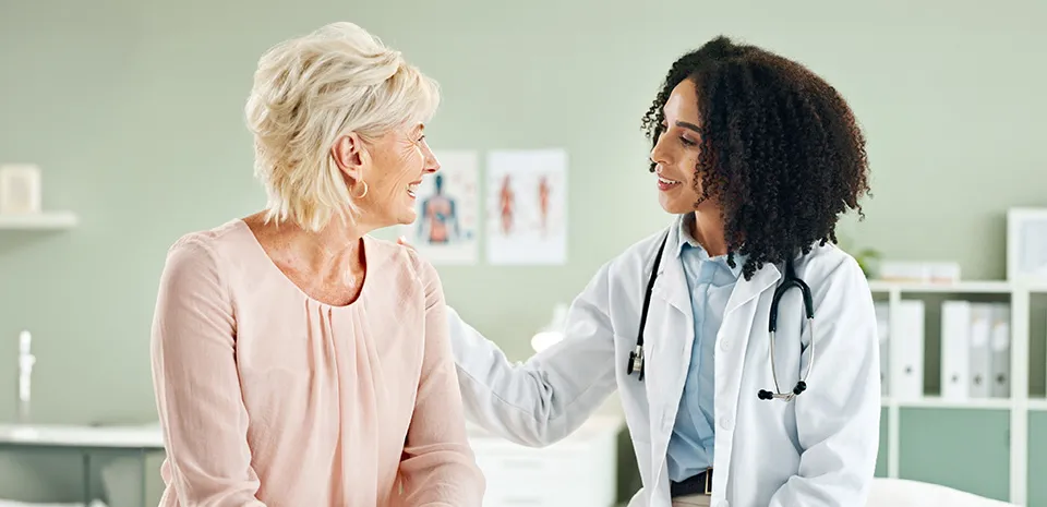 A patient and doctor are having a conversation while the doctor touches the patient's shoulder, highlighting a warm welcome for patients.