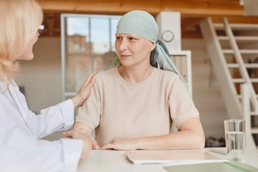Woman with cancer wearing head cover is comforted by an oncology nurse navigator