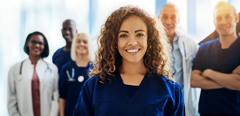A woman in scrubs stands in front of a group of other health care workers representing those who would like to work for UMass Memorial Health.