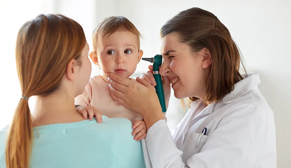 A doctor looking into a child's ear while the child is held by a parent.