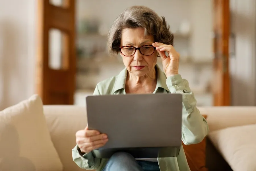 older woman with cataracts wearing glasses struggling to look at a computer.