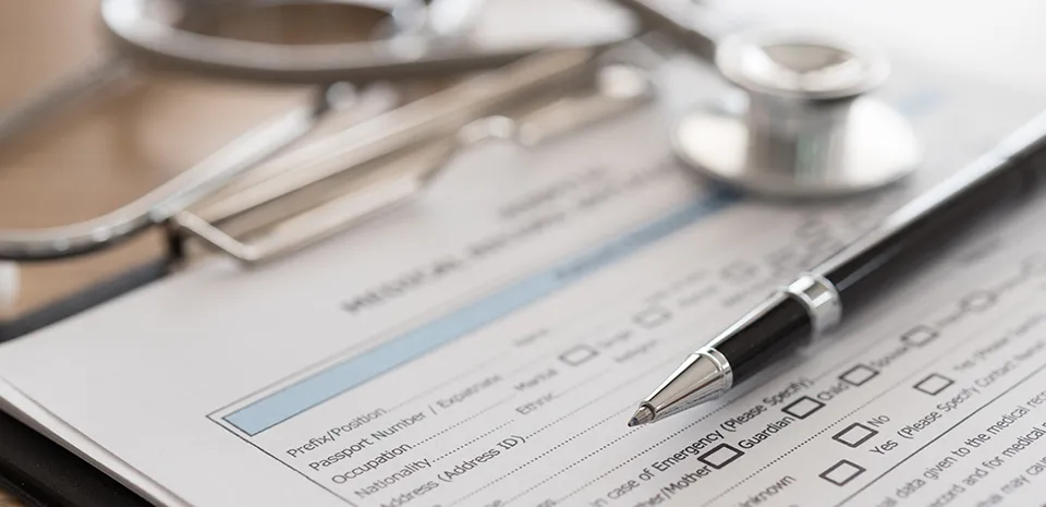 A pen and a stethoscope are laying on top of a form in a clipboard. 
