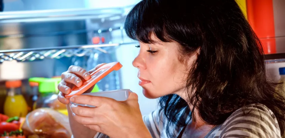 woman smelling a container to see if food has spoiled