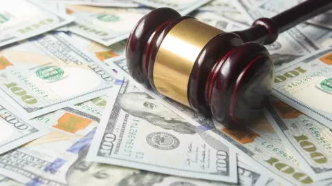 A judge's gavel lays on top of a pile of money, representing this court case.