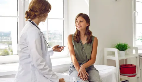 A caregiver speaks with a patient sitting on a bed.