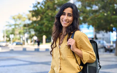Student intern with long, dark, wavy hair wearing a mustard yellow button-up dress shirt with a backback over her shoulder