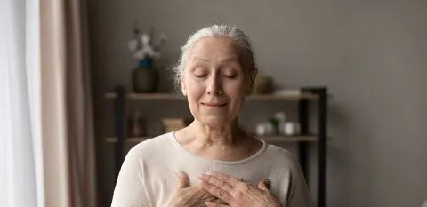 elderly woman mediating with hands over her heart