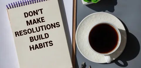 Cup of coffee next to paper with words Don't Make Resolutions, Build Habits