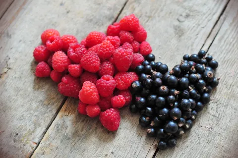 A red raspberry heart is next to a black currant heart on a wooden table.