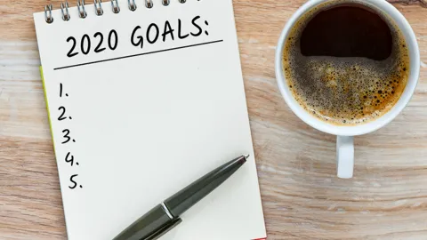 A coffee sits next to a checklist of 2020 goals.
