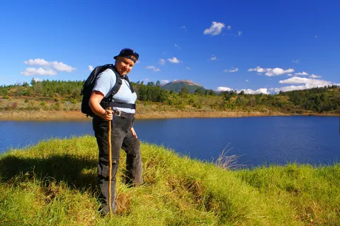A mature woman is hiking and posed in front of a lake and mountains.