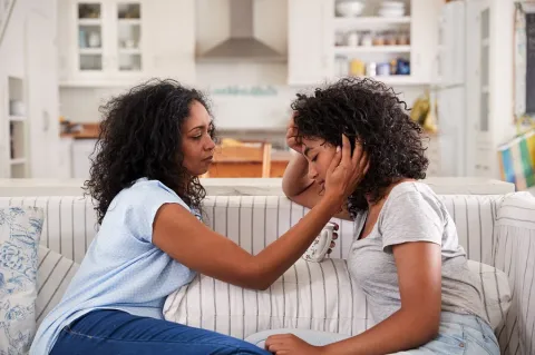 A woman is comforting a teenager on a couch.
