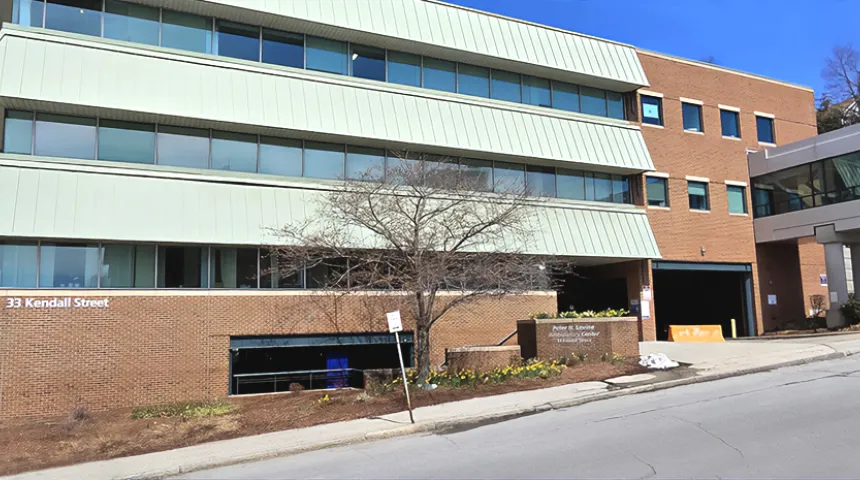 A red brick building with green awnings on each floor, against a blue sky. 33 Kendall Street is on the side of the building of the Peter H Levine Ambulatory Center at UMass Memorial Medical Center - Memorial Campus.