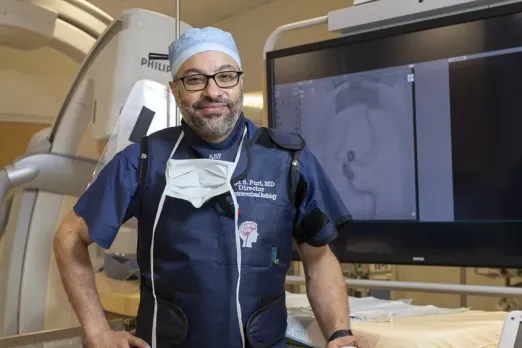 Ajit Puri, MD, stands in front of medical equipment that performs imaging needed for minimally invasive endovascular procedures to treat strokes and aneurysms.