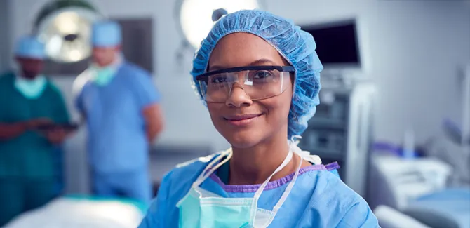 A CRNA in an operating room, smiling and looking at the camera.