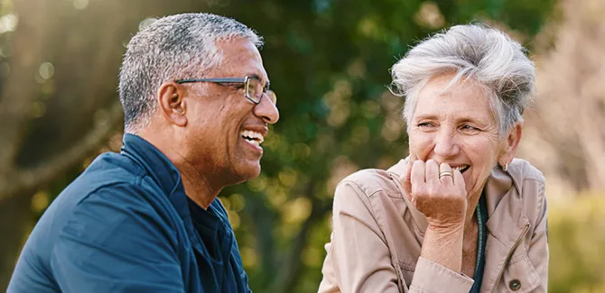 A happy older couple smiles and shares a laugh outdoors on a beautiful day.