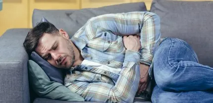 A man laying on a couch, holding his stomach in discomfort.