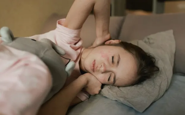 young girl with measles lying in a bed with eyes closed