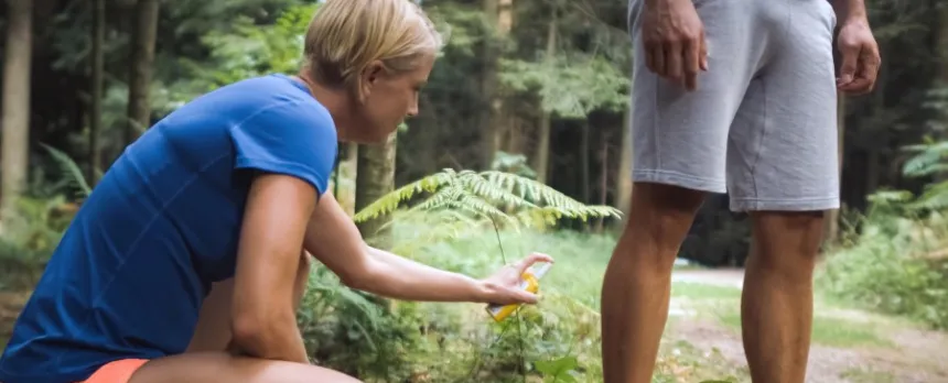 Woman bending down putting bug spray on a man's legs while hiking in the woods.