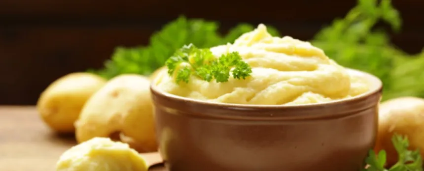 a brown bowl with vegan mashed potatoes and parsley and raw potatoes next to it.