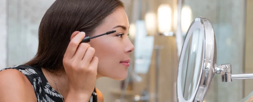woman looking in mirror putting mascara on