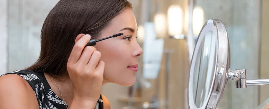 woman looking in mirror putting mascara on
