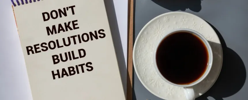 Cup of coffee next to paper with words Don't Make Resolutions, Build Habits