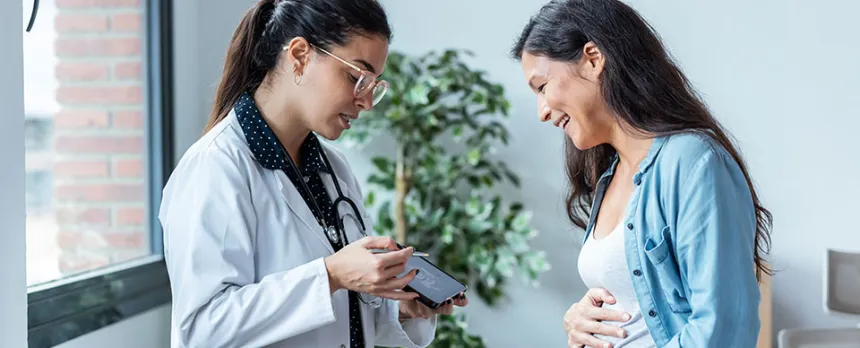 A doctor on the left showing a patient on the right a picture of an ultrasound. The patient on the right holds her stomach, smiling at the ultrasound.